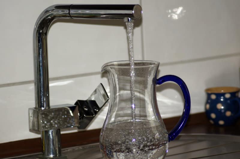 Water flows from a modern faucet into a glass pitcher with a blue handle