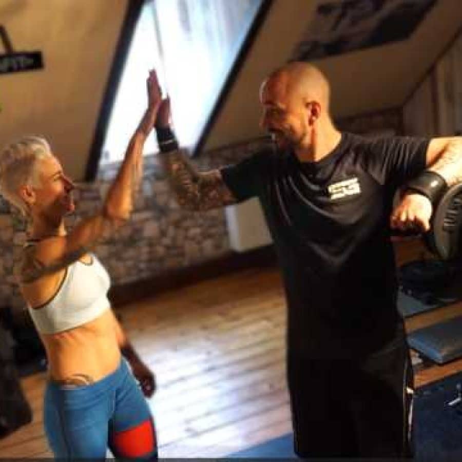 Éowyn und Mike feiern einen erfolgreichen Trainingstag mit einem High-Five in Ihrem Fitnessraum.