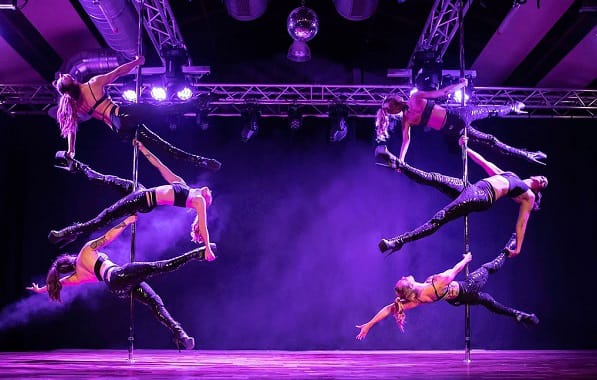 Pole Dance Show: Faszinierende Kunst und atemberaubende Akrobatik 11 Eine Gruppe von Pole-Dance-Athletinnen präsentiert eine synchronisierte Performance bei einer Meisterschaft, in einer eindrucksvoll beleuchteten Bühnenszene.