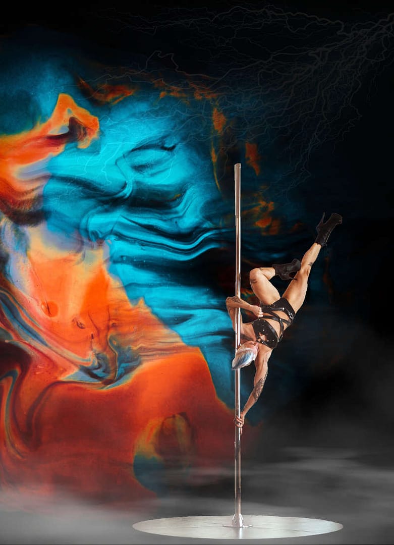 Verführerischer Tanz an der Stange: 5 unglaubliche Fakten 1 Poledance-Performance vor einem kunstvollen, farbenfrohen Hintergrund. Die Tänzerin zeigt eine akrobatische Pose an der Stange und kombiniert Stärke mit Eleganz.